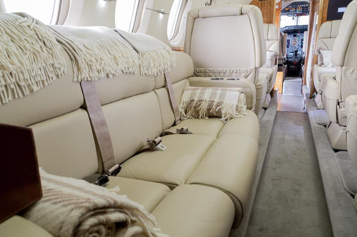 The luxurious cabin interior of a private jet with cream leather seating and soft blankets.