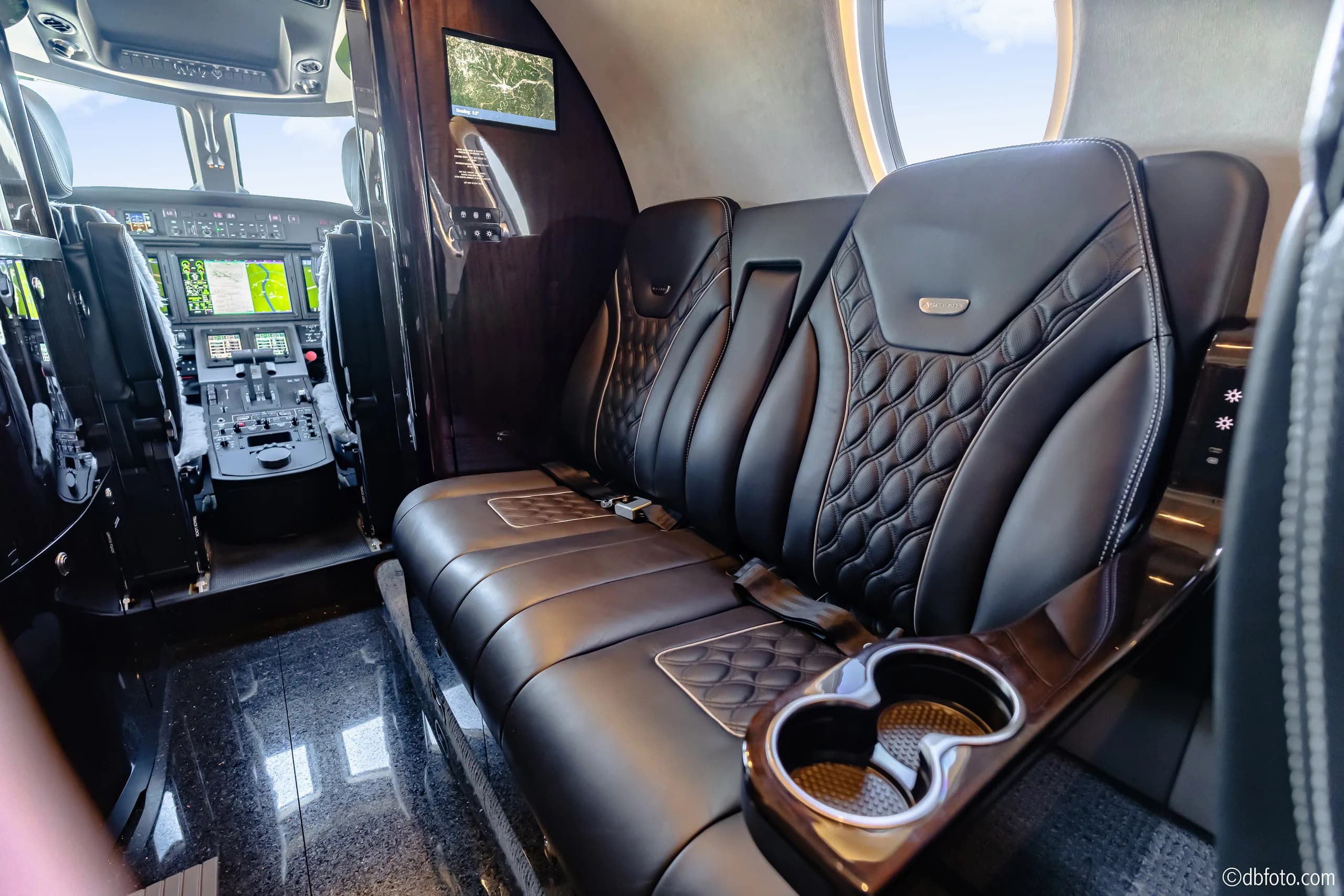 A view inside the business jet's cabin, highlighting the black quilted leather seating and a cup holder.