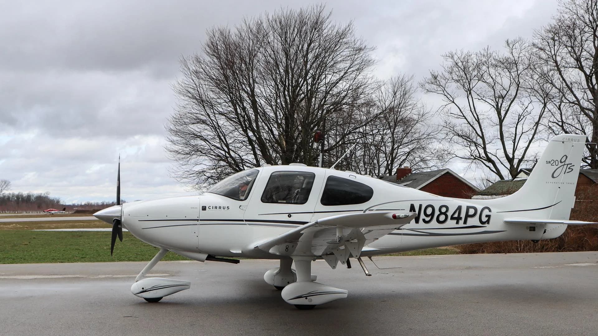 A white Cirrus SR20 GTS aircraft, N984PG, is parked with its right side visible on a cloudy day.