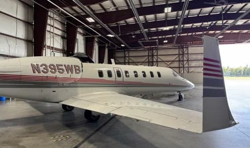 A close-up side view of a white Learjet 35A business jet with red and grey stripes, registration N395WB, parked in a hangar.