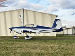 A blue and white aircraft with registration LY-BTY is parked on the ground near a building.
