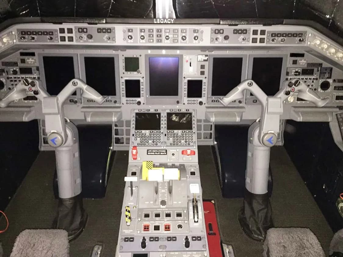 The modern cockpit of a Legacy aircraft, featuring multiple digital displays and a complex control panel.