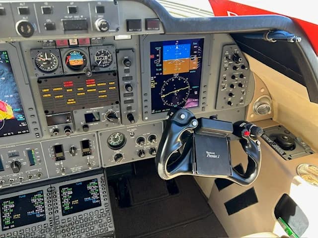A close-up of the right side of a business jet's cockpit, showing the instrument panel, digital displays, and control yoke.