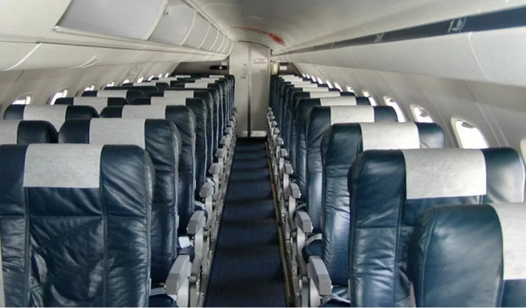 A long view down the aisle of an aircraft cabin with rows of dark blue seats with light grey headrests.