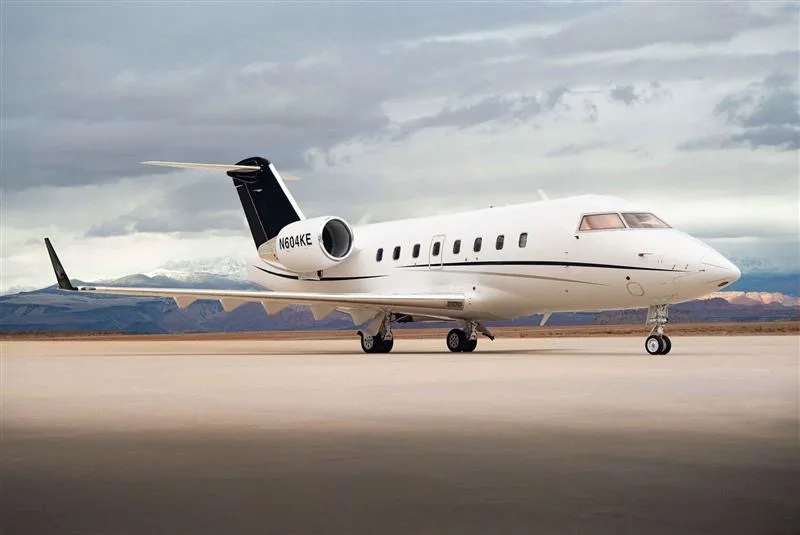 A Challenger aircraft is parked on the tarmac with mountains in the background.