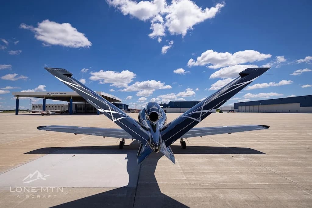 A rear view of a black Cirrus Vision Jet (N247CF) showcasing its V-tail design and engine intake on an airport tarmac.