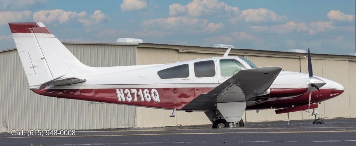 A side view of a white and red twin-engine propeller aircraft with registration N3716Q, parked next to a metal hangar.