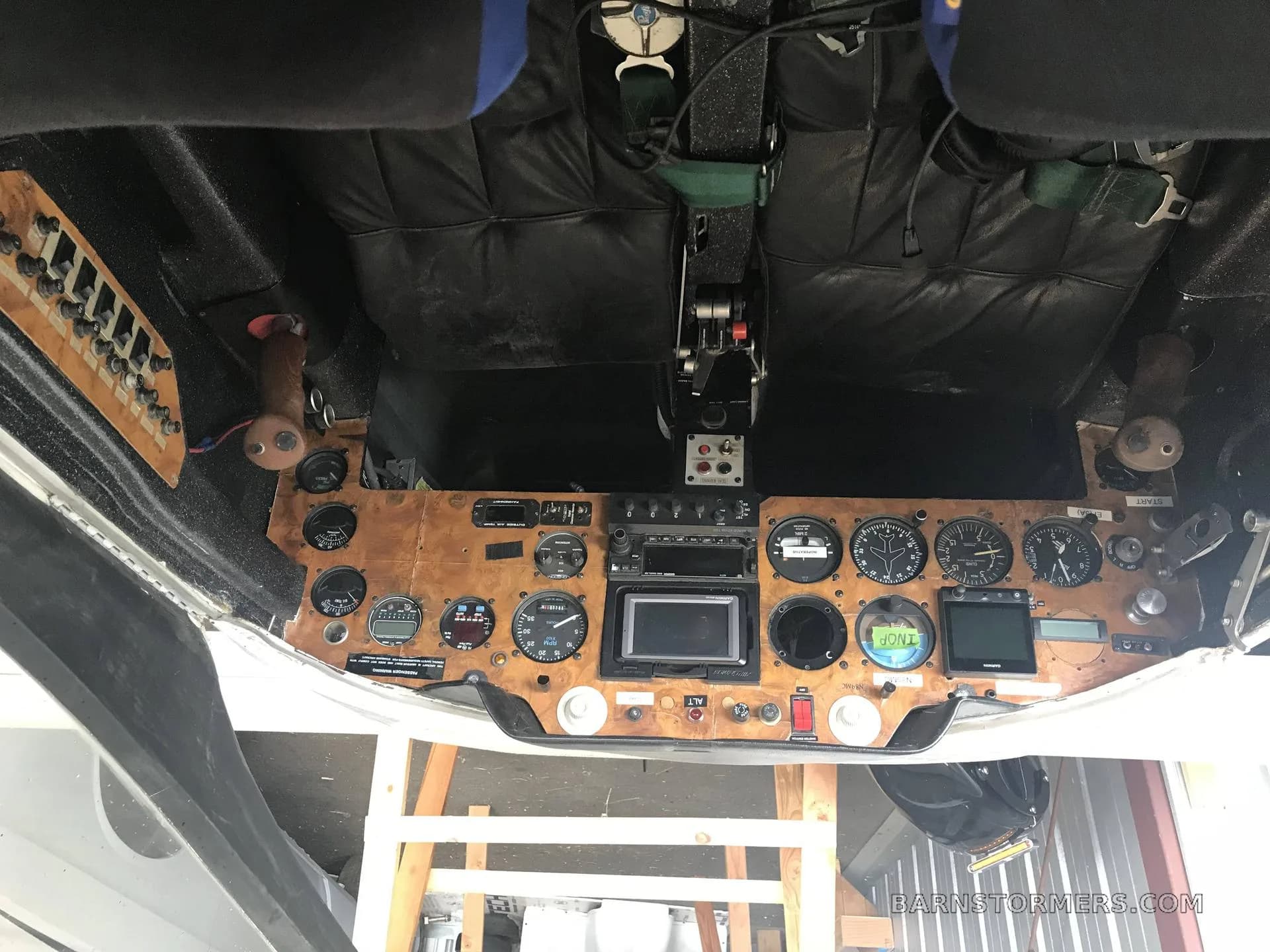 An upside-down view of a cockpit with a wooden instrument panel, various gauges, screens, and a control stick.