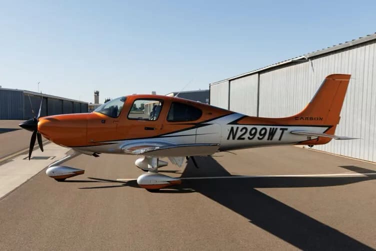 Side view of an orange and silver Cirrus SR22T GTS aircraft with registration N299WT parked on an tarmac.