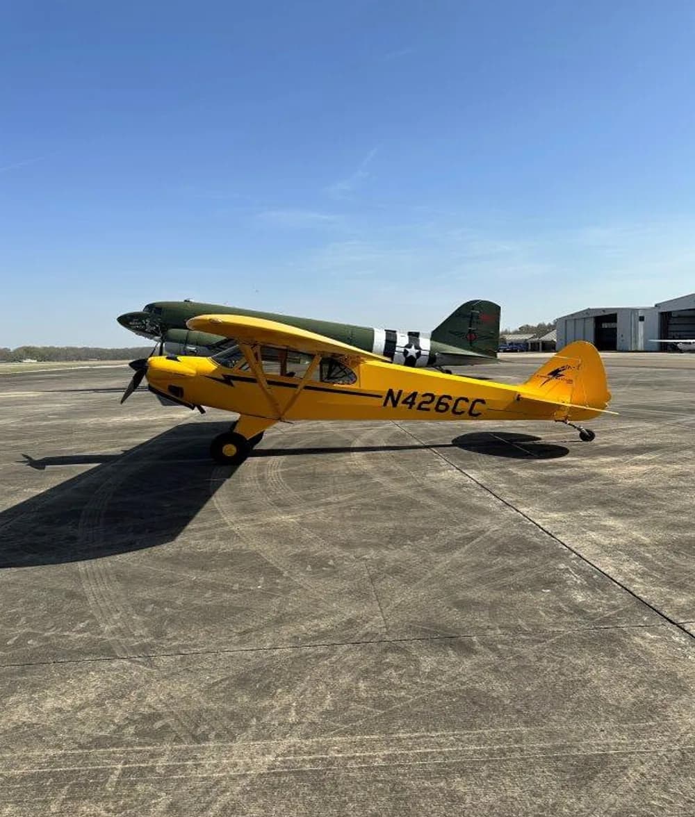 A yellow Carbon Cub aircraft, registration N426CC, parked on the tarmac with another aircraft in the background.