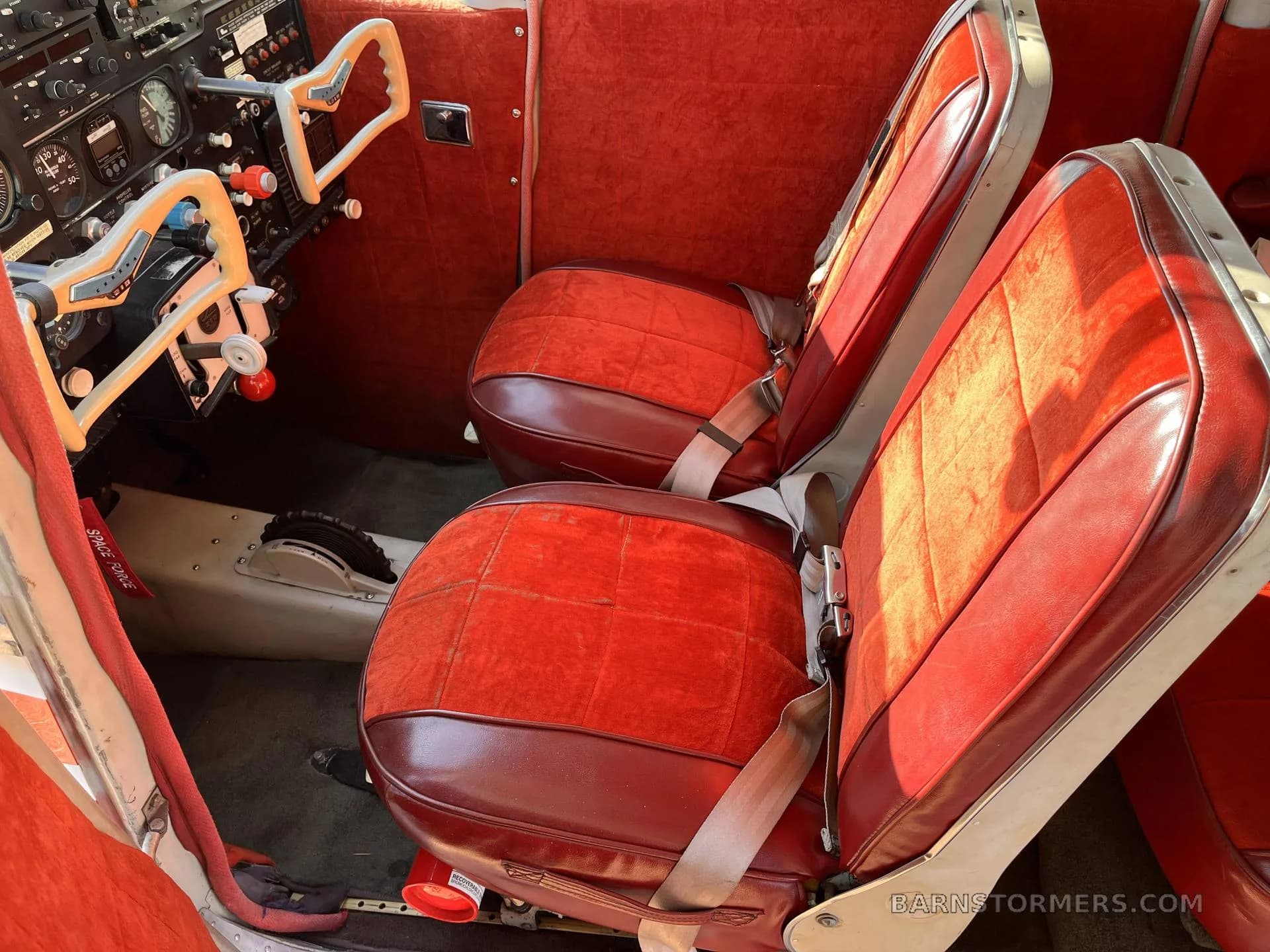 The red upholstered front seats and part of the cockpit of a Cessna 182 aircraft.