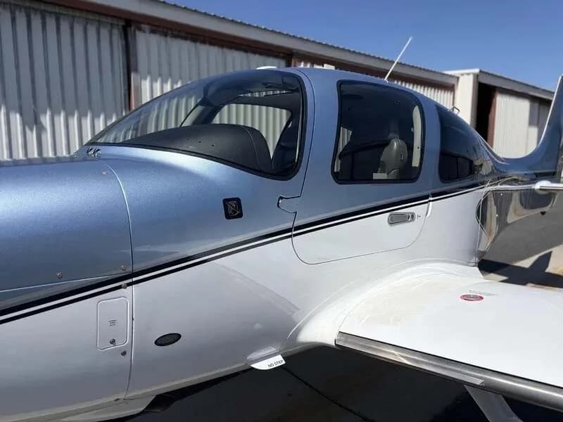 A close-up side view of the cockpit and wing root of a blue and white Cirrus SR22 aircraft.