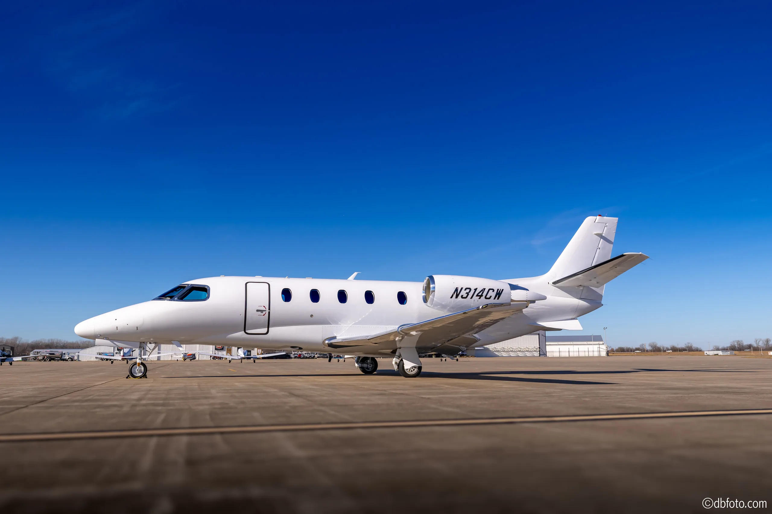 A white business jet, N314CW, is parked on an airport tarmac under a clear blue sky.