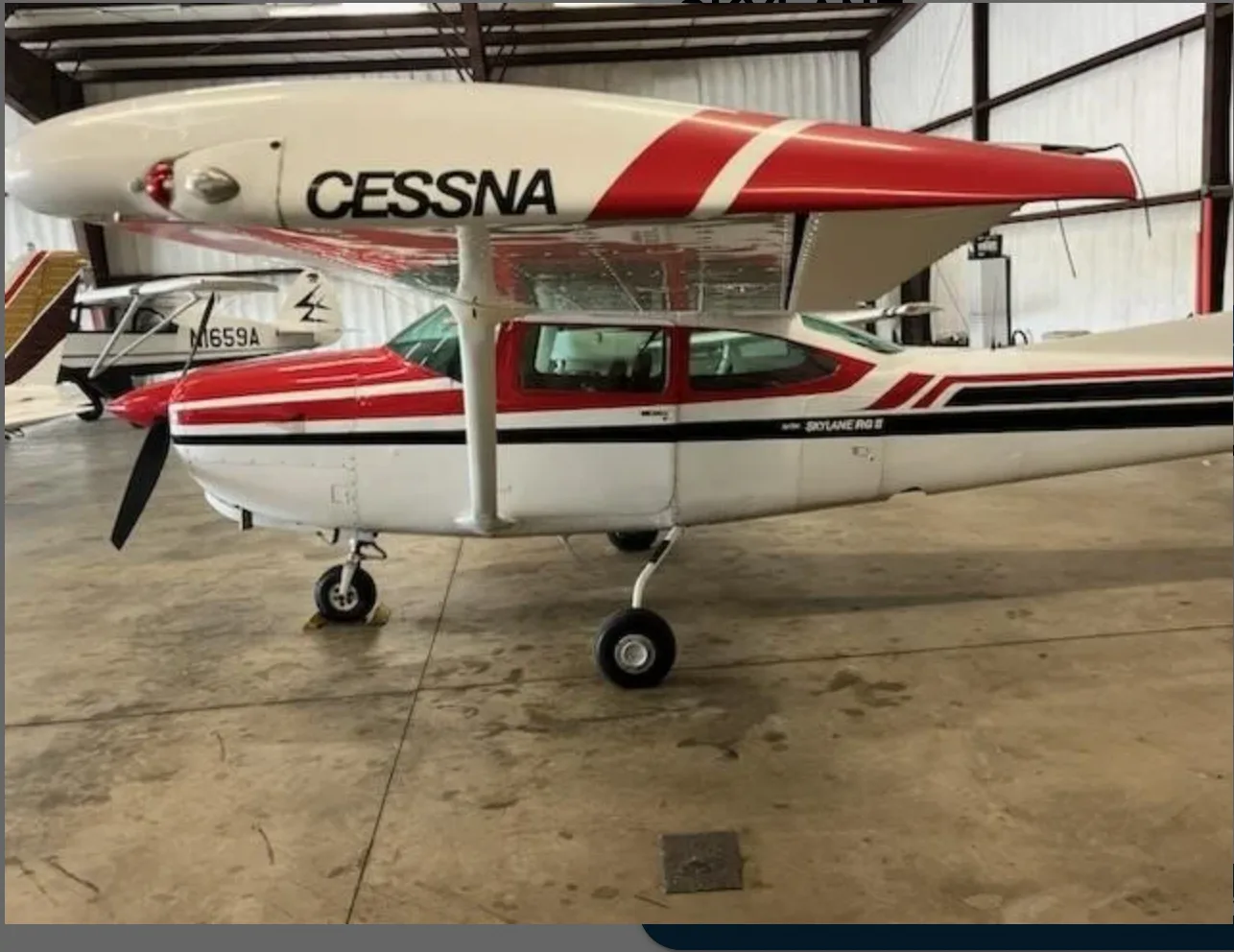 A red and white Cessna 182 Skylane parked inside a hangar, viewed from the front-left.