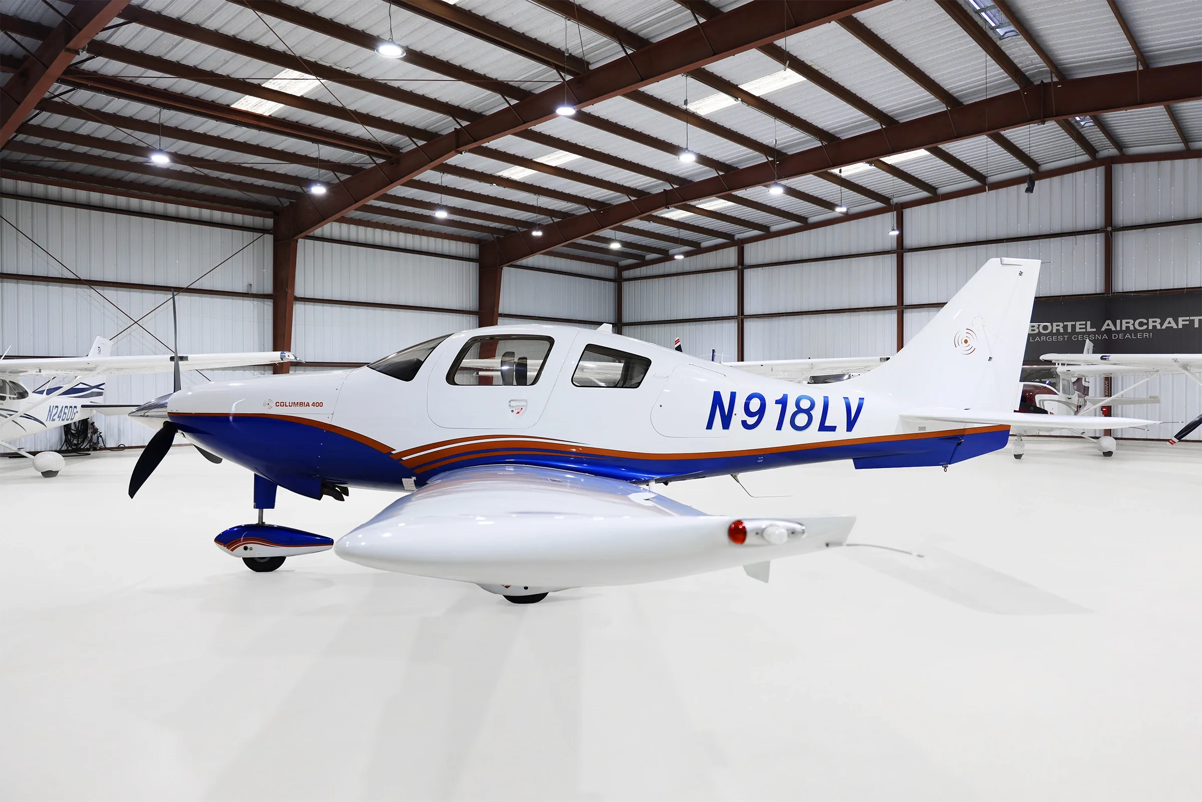A white and blue Columbia 400 aircraft with registration N918LV is parked in a hangar, viewed from the right side.