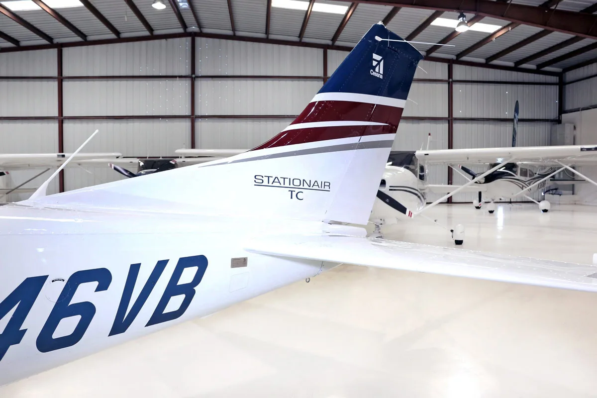 A close-up view of the tail of a white and blue Cessna Stationair TC aircraft (N46VB) with maroon accents, parked in a hangar.