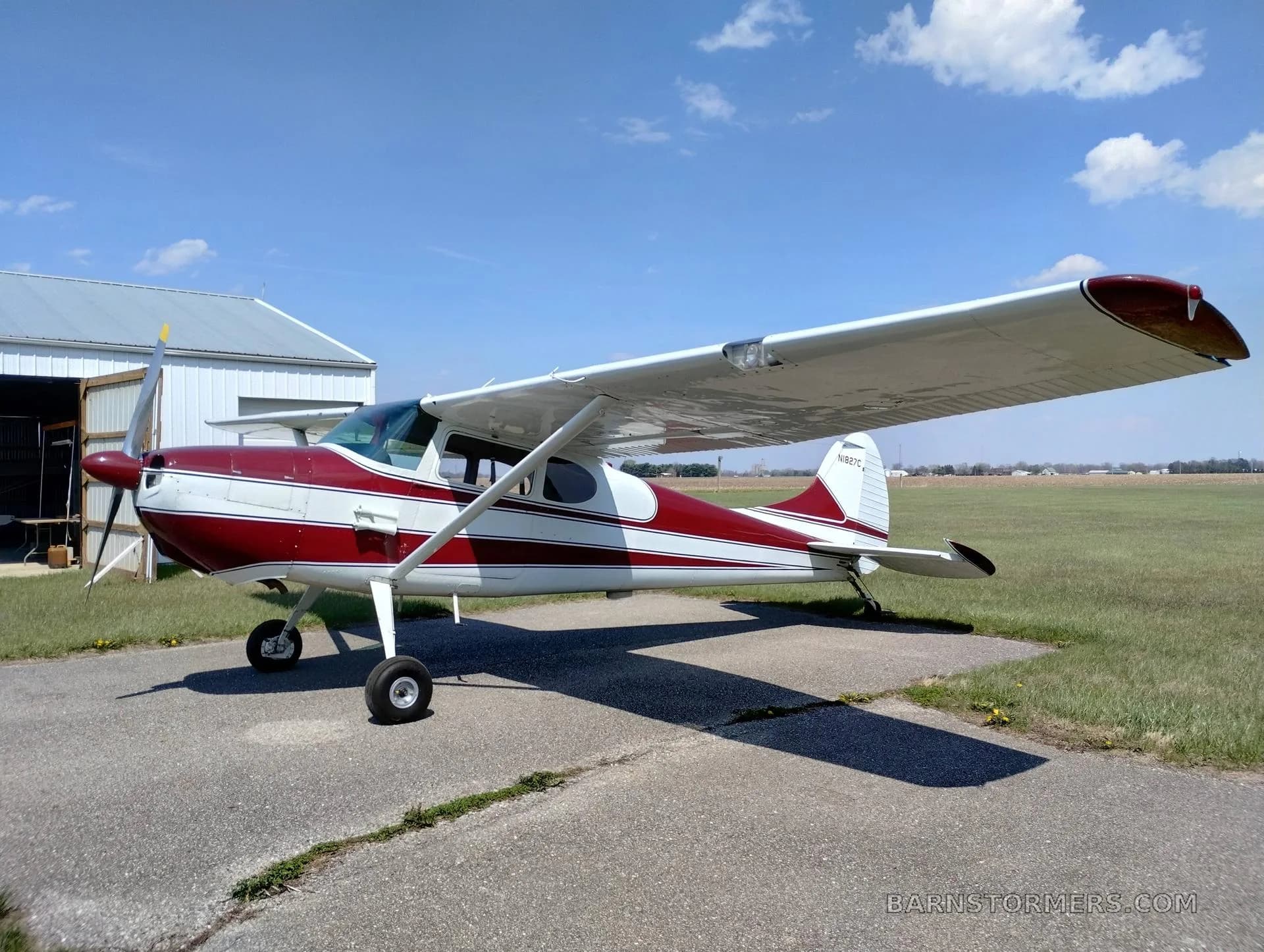 A red and white single-engine propeller aircraft with tail number N1827C is parked on an asphalt pad with a hangar in the background.