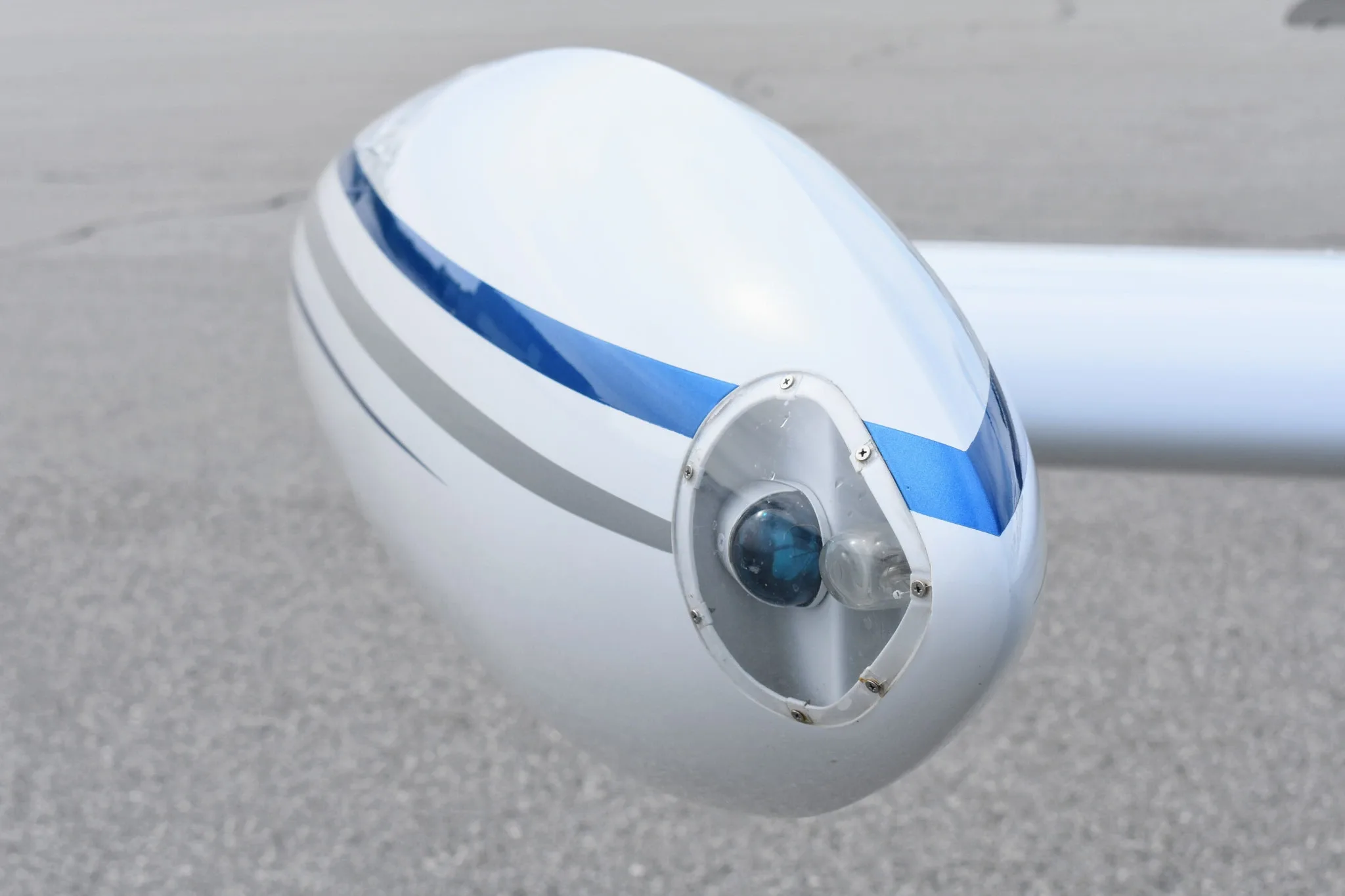 A close-up of the white wingtip of a Beechcraft Bonanza F33A with blue and grey stripes and a landing light.