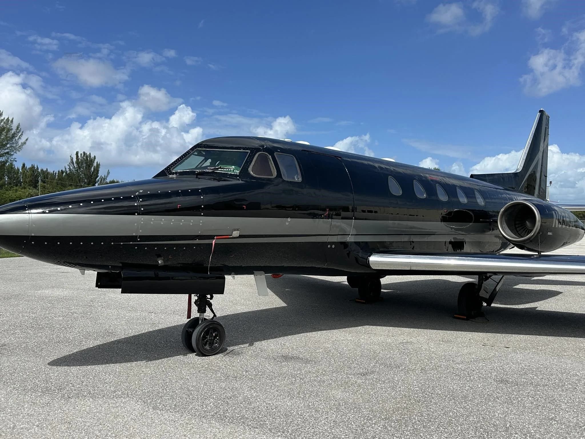 A side view of a black and silver business jet parked on an asphalt tarmac under a partly cloudy sky.