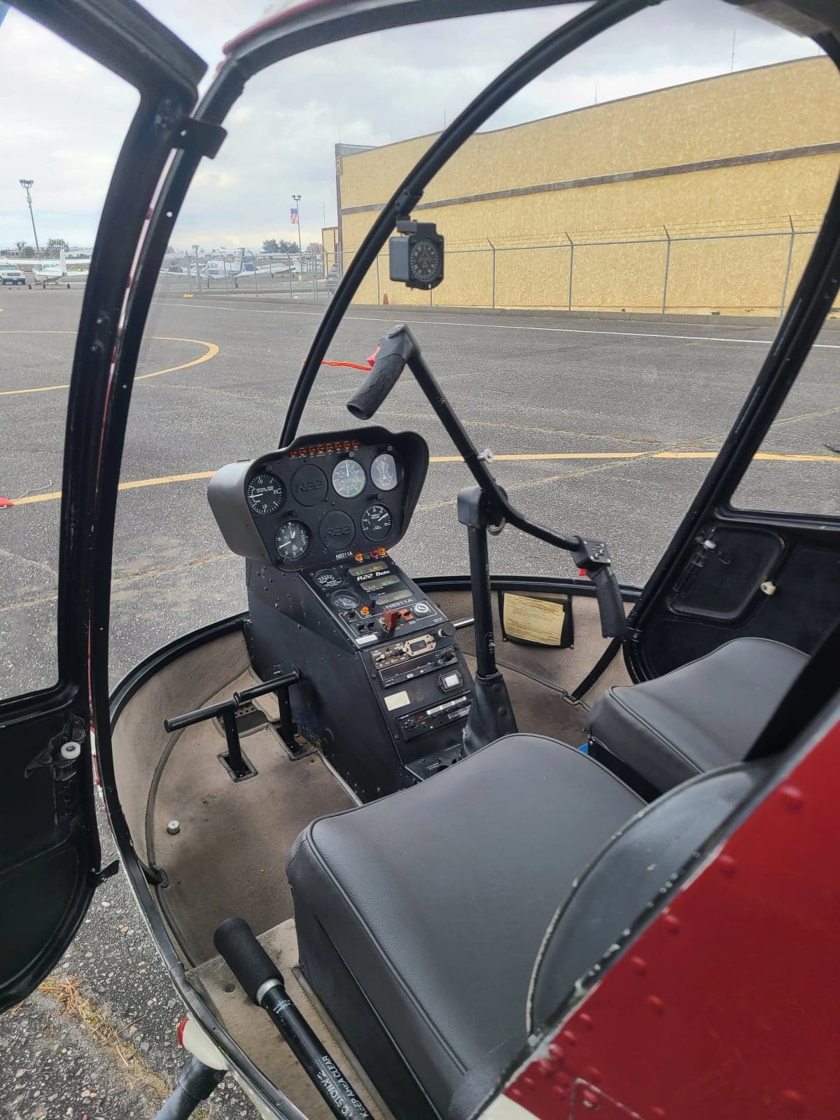 The interior of a Robinson R22 Beta helicopter, showing black seats and the cockpit controls from an open door.