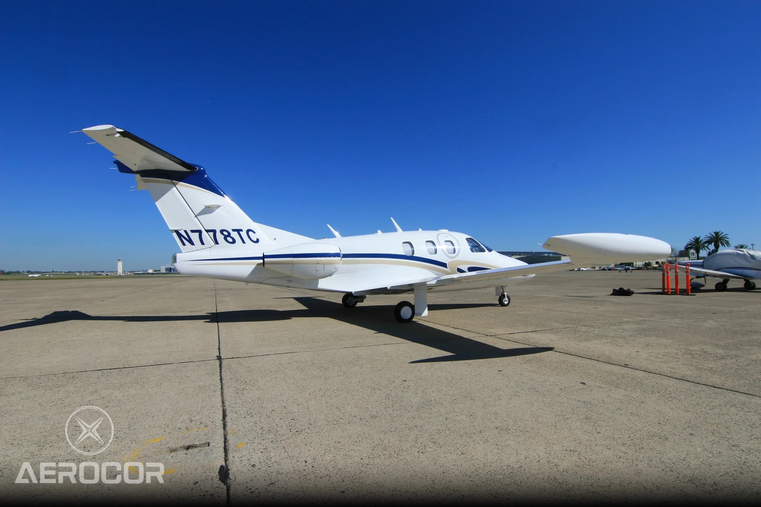A white Eclipse 500 jet with blue and gold stripes, viewed from the front-right on the tarmac.