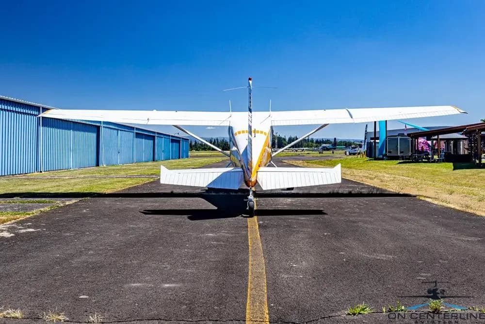 A rear view of a white and orange Cessna 185 Skywagon (N1841R) parked on an asphalt ramp.