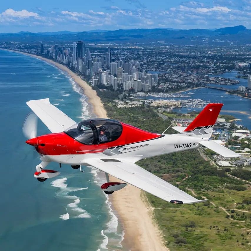 A red and white light aircraft flying over a coastal city.