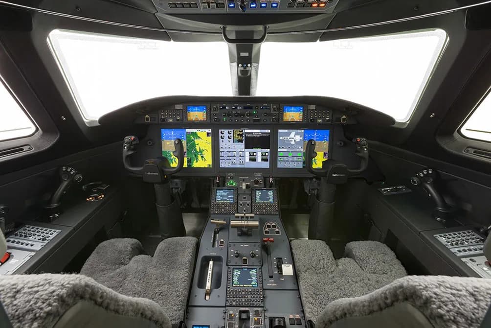 The modern cockpit of a private jet, featuring multiple digital displays, control yokes, and a central throttle quadrant.