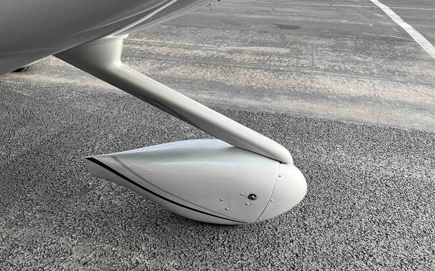 A close-up view of the main landing gear fairing of a silver Cirrus SR22 aircraft on asphalt.