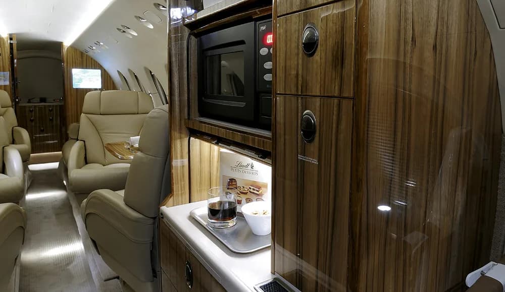 A view of the business jet's galley area with a microwave and elegant wooden cabinetry.