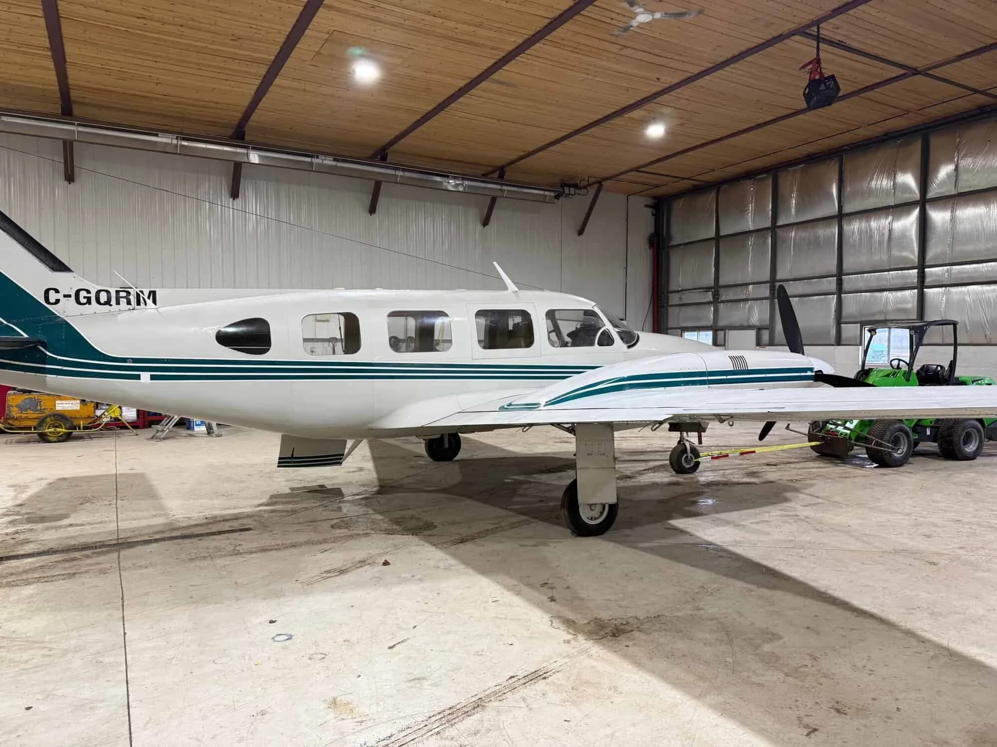 A white and green twin-engine aircraft, registration C-GQRM, viewed from the side in a hangar.