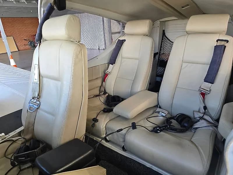 The aircraft's interior shows cream-colored leather seats with headsets.
