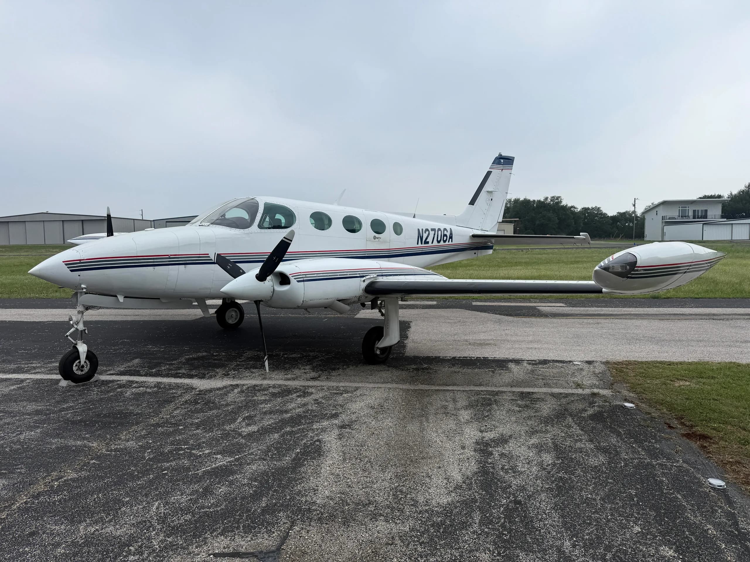 A white Cessna 335 aircraft, registration N2706A, with blue and red stripes, parked on an airfield.