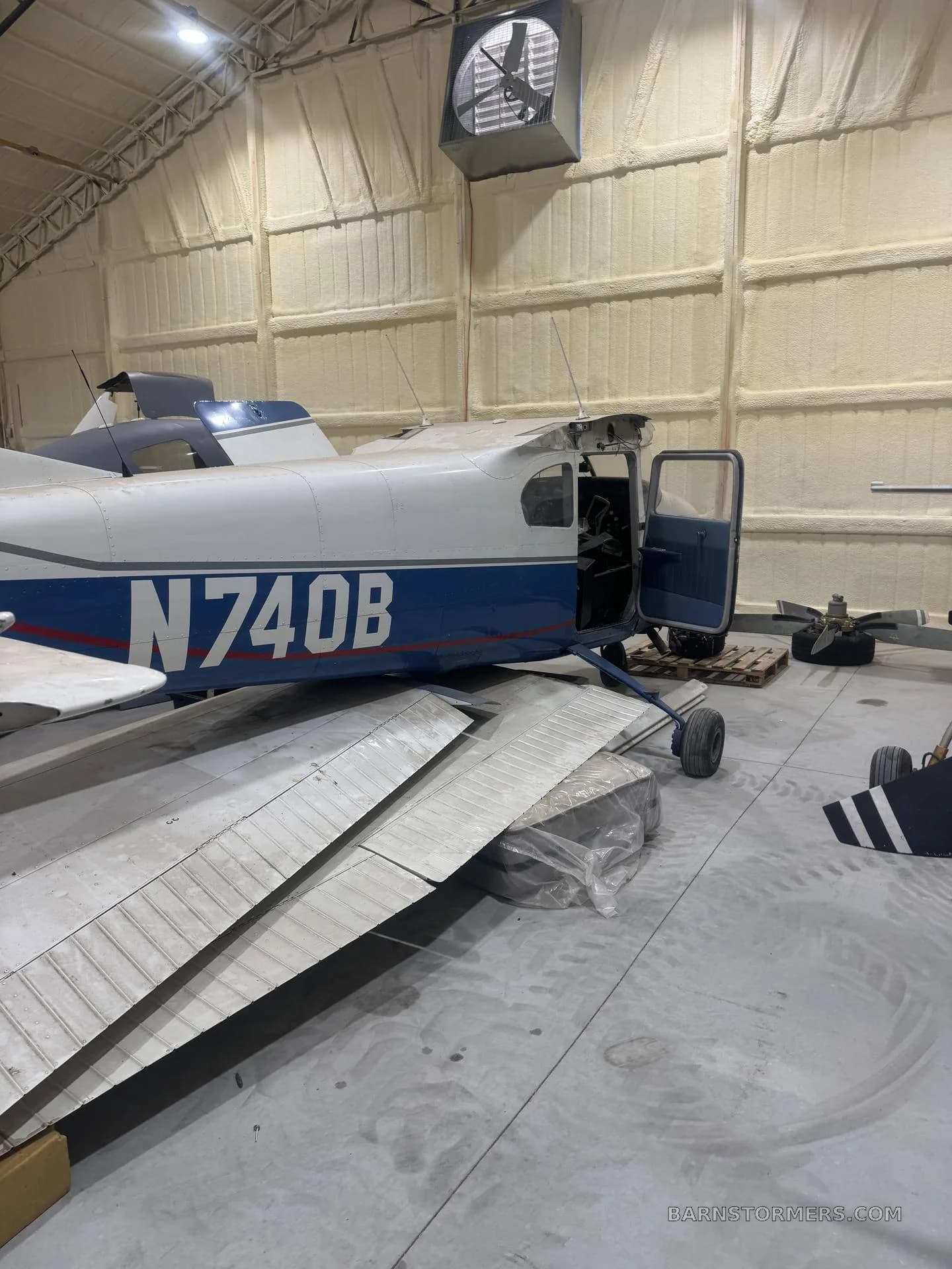 A partially disassembled blue and white single-engine aircraft (N740B) with its wing removed, inside a hangar.