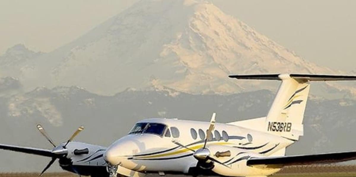 Beechcraft King Air with a white and gold paint scheme in front of a mountain.