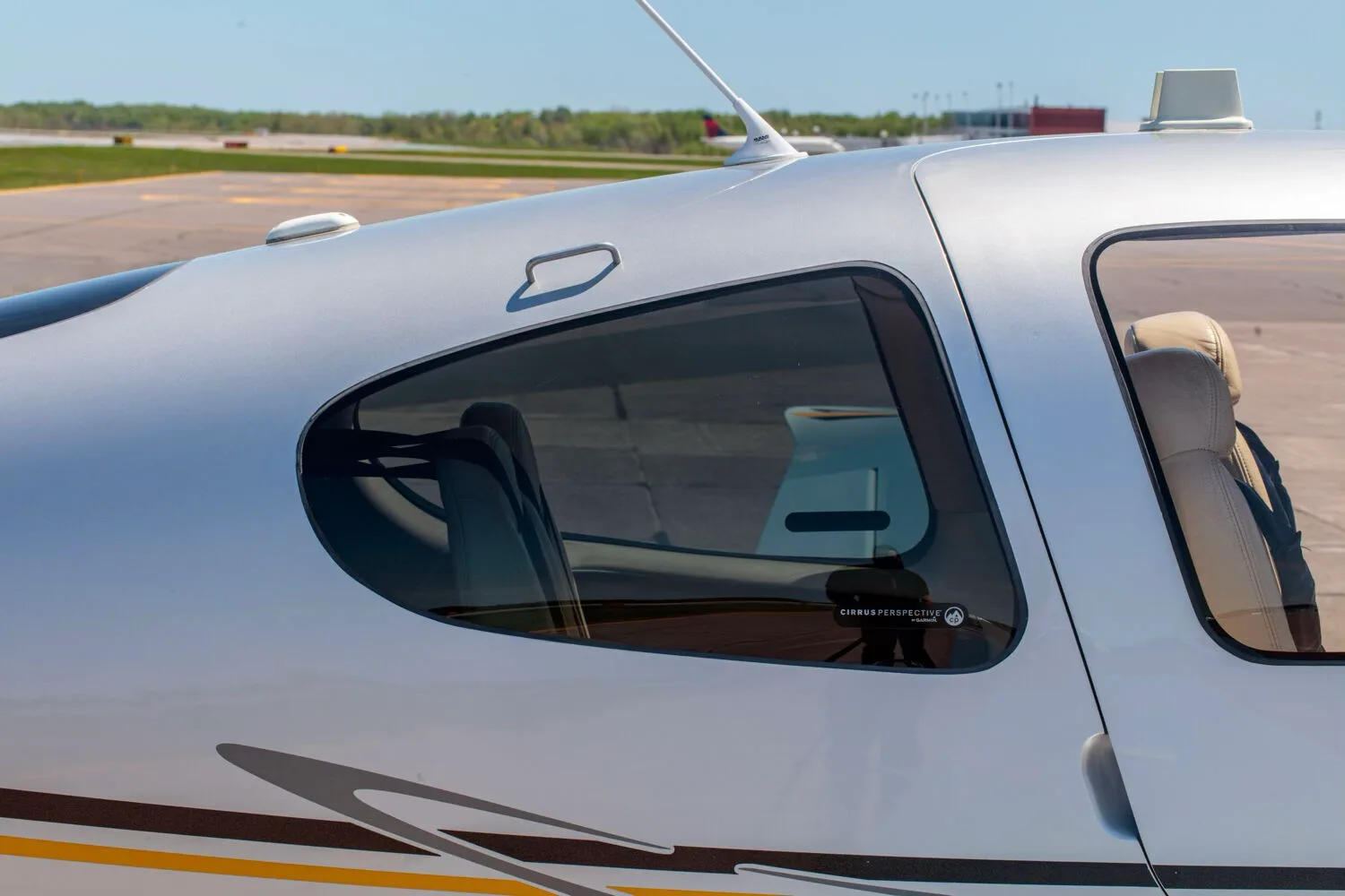 A close-up view of the cabin window and antenna on the fuselage of the silver Cirrus SR22T aircraft.