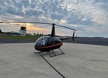 Robinson R44 Raven II helicopter on the tarmac at sunset.