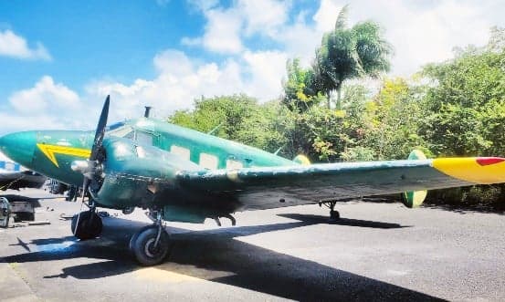 A Lockheed Model 10 Electra aircraft with a green and yellow paint scheme is parked on the tarmac.