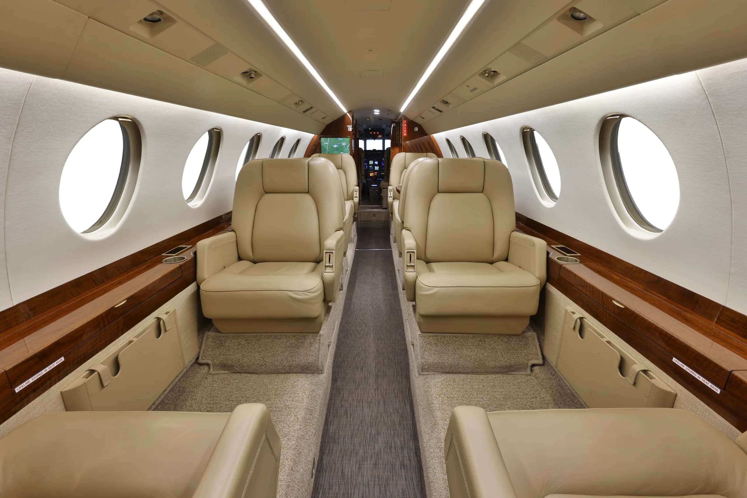 A wide view of the business jet's cabin shows beige leather seating, wood trim, and a central aisle.