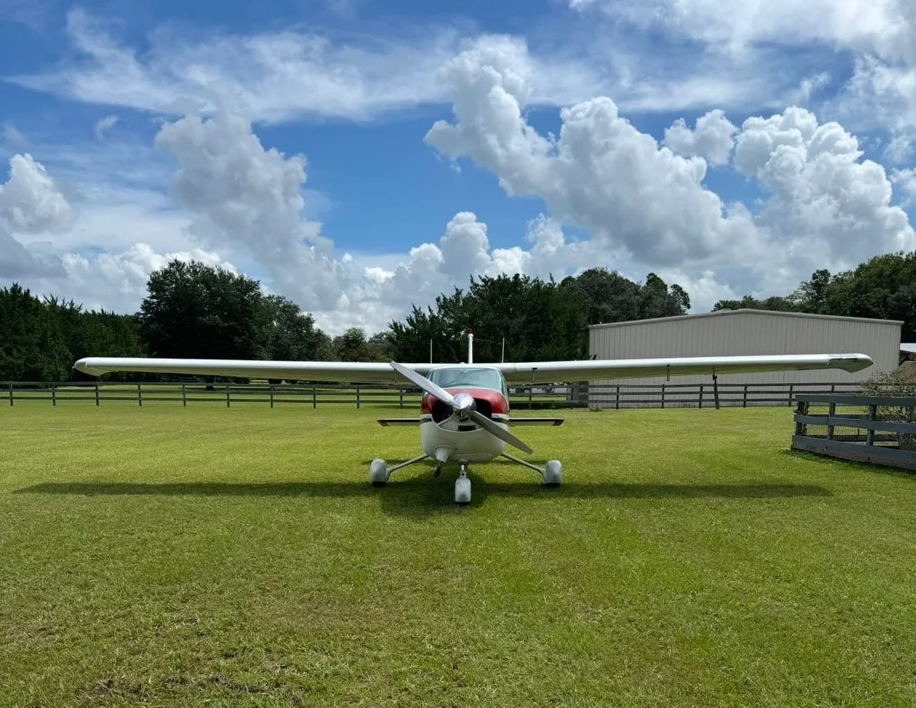 A white Cessna 182 with red and blue stripes viewed head-on, parked on a green grassy field.