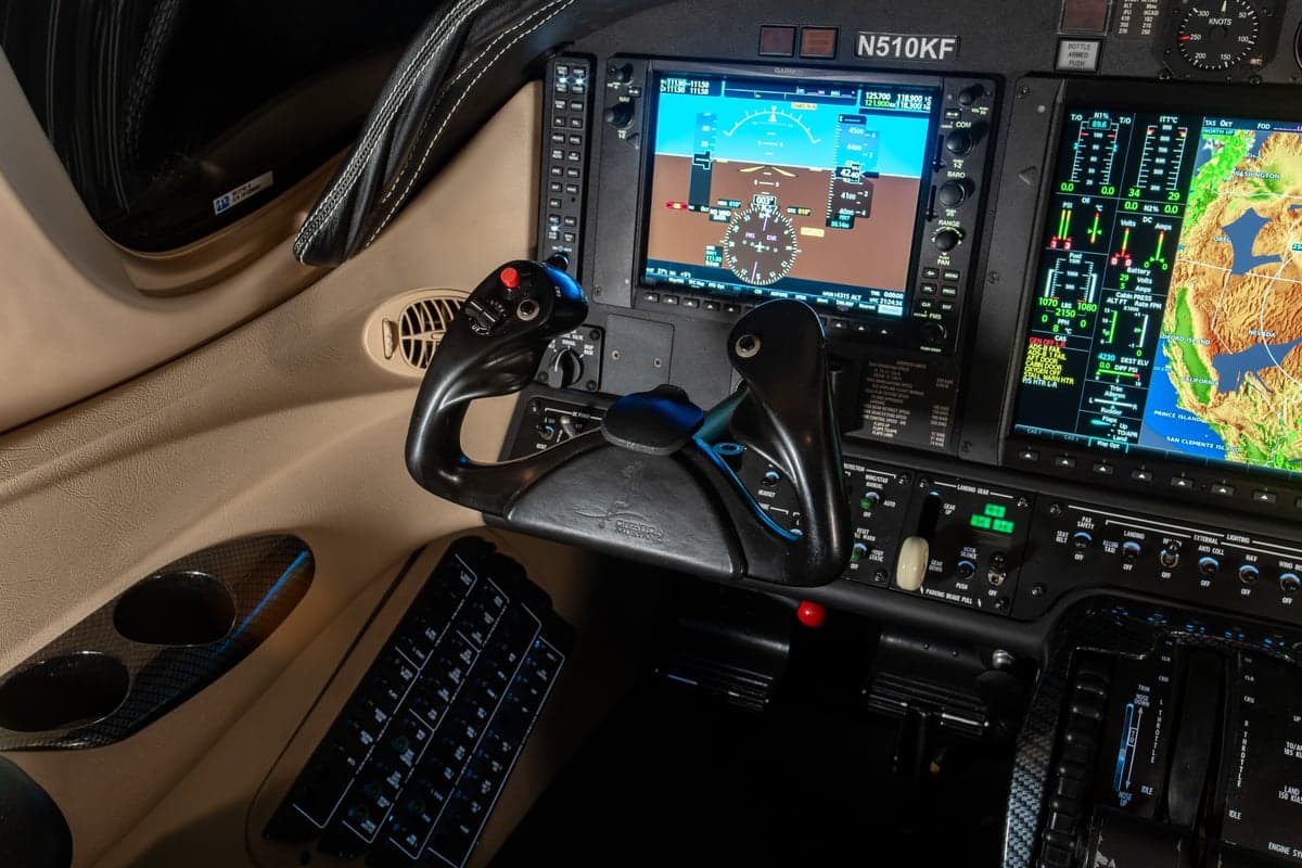 A close-up view of the cockpit of a Cessna Citation M2, showing the pilot's yoke and multi-function displays with navigation data.