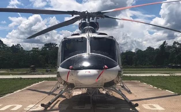 A front view of a red, white, and black Bell 412 helicopter on a helipad under a cloudy sky.