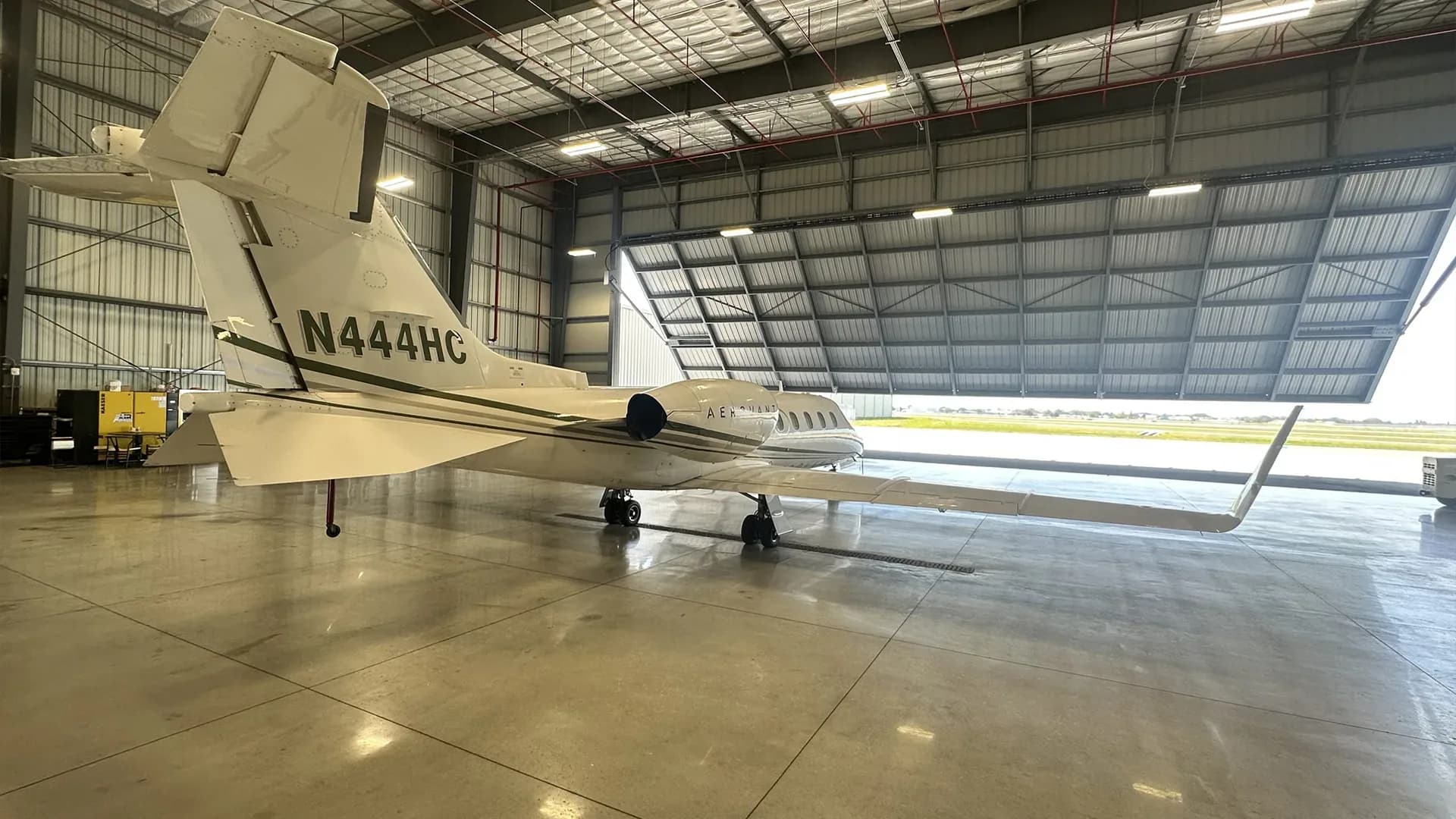 The tail of a Learjet 25D aircraft is visible inside a hangar, showing the tail number N444HC.