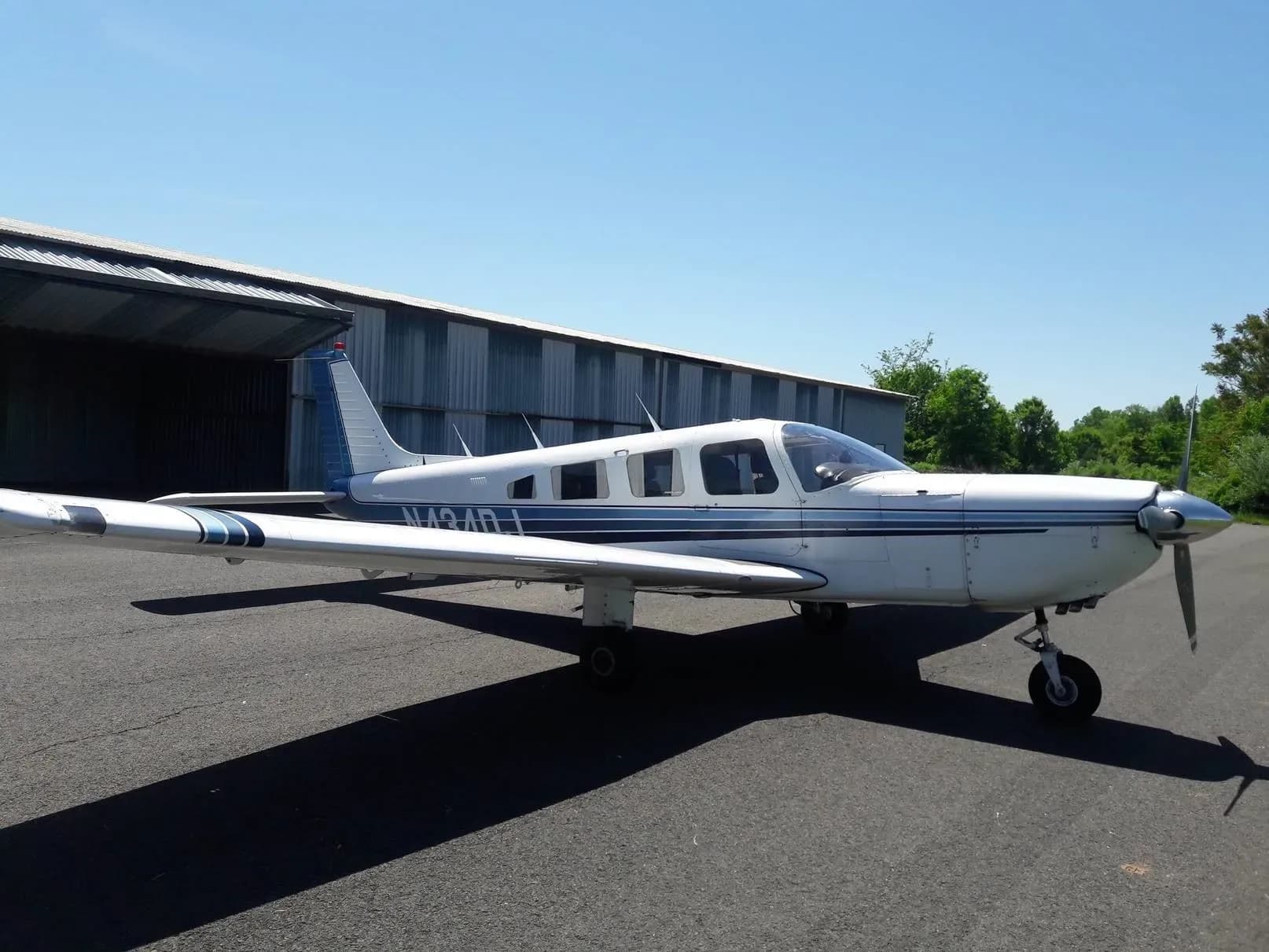 A front-side view of the white Piper PA-32R-300 Cherokee Lance, registration N434DJ, parked on an airfield next to a hangar.