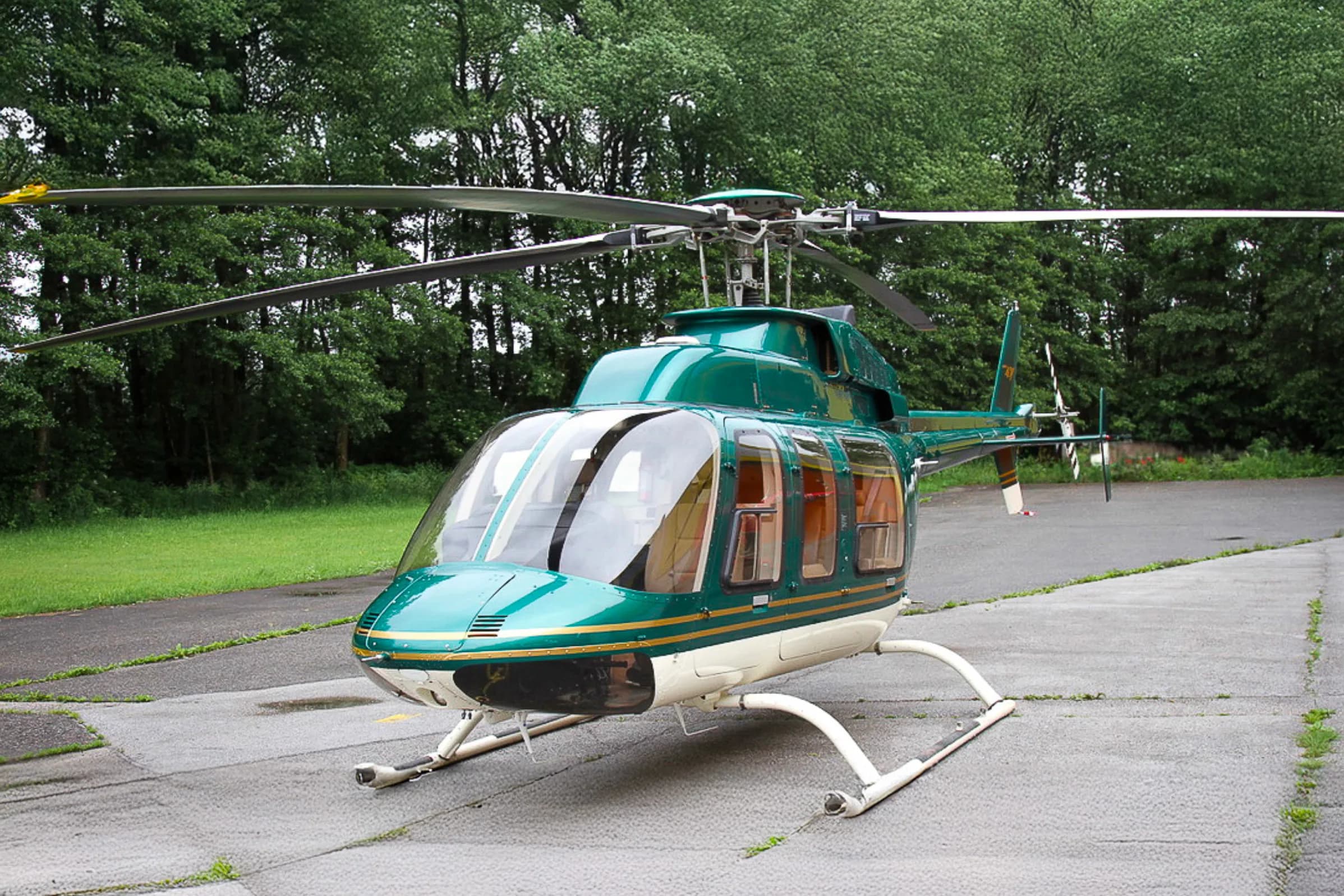 A Bell 407 helicopter with a green and white paint scheme is parked on the tarmac.