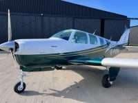 A Beechcraft Bonanza with a white and green paint scheme is parked on the tarmac.
