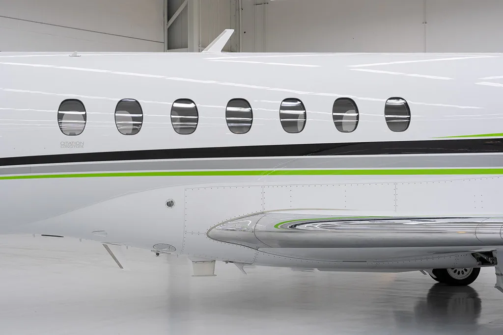 A close-up side view of the fuselage of a Citation Longitude business jet, showing its windows and green and black stripe livery.