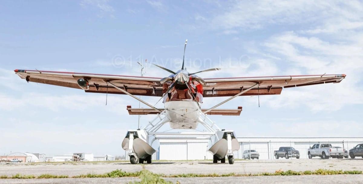 A rear view of the red and white Kodiak 100 seaplane with floats, parked on an airfield.