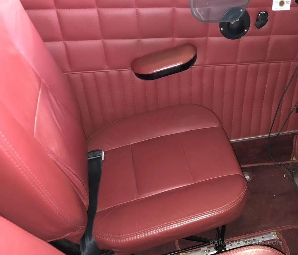 A single red leather aircraft seat with quilted side paneling and an armrest.