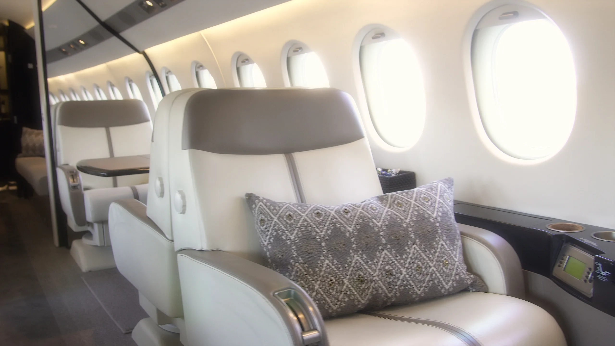 A close-up view of a light-colored leather cabin seat with a patterned pillow next to a window.